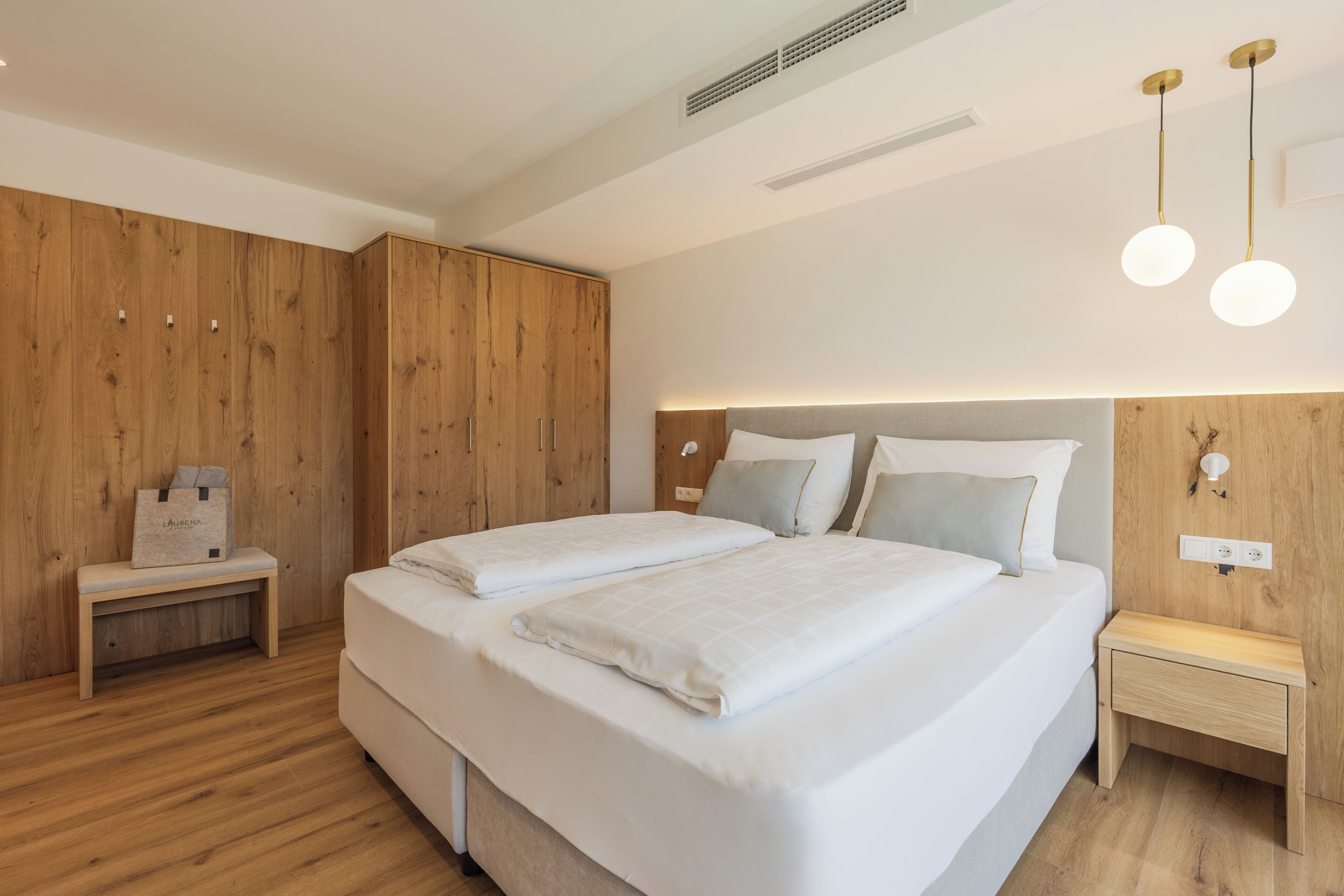 Une chambre moderne avec un grand lit, des tables de chevet, un banc et un lambris en bois.