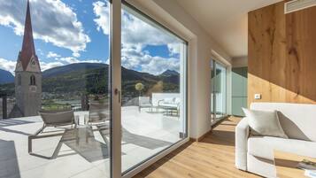 Un interior moderno con un gran ventanal corredero que da a una terraza exterior con vistas a una iglesia y montañas.
