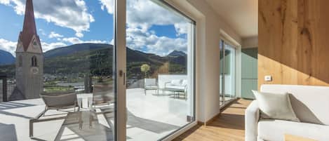 A modern interior with a large sliding glass door leading to an outdoor terrace with a view of a church and mountains.