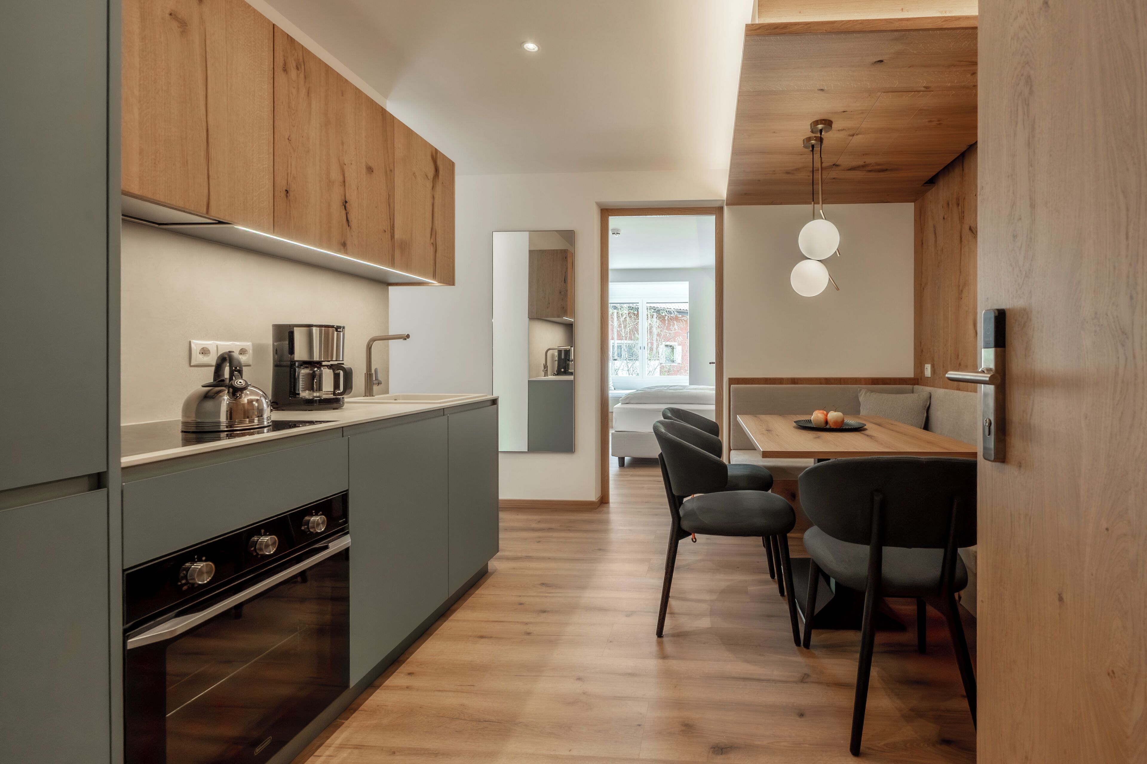 A modern kitchen with wooden cabinets, a built-in oven, and a dining area with a wooden table and chairs.