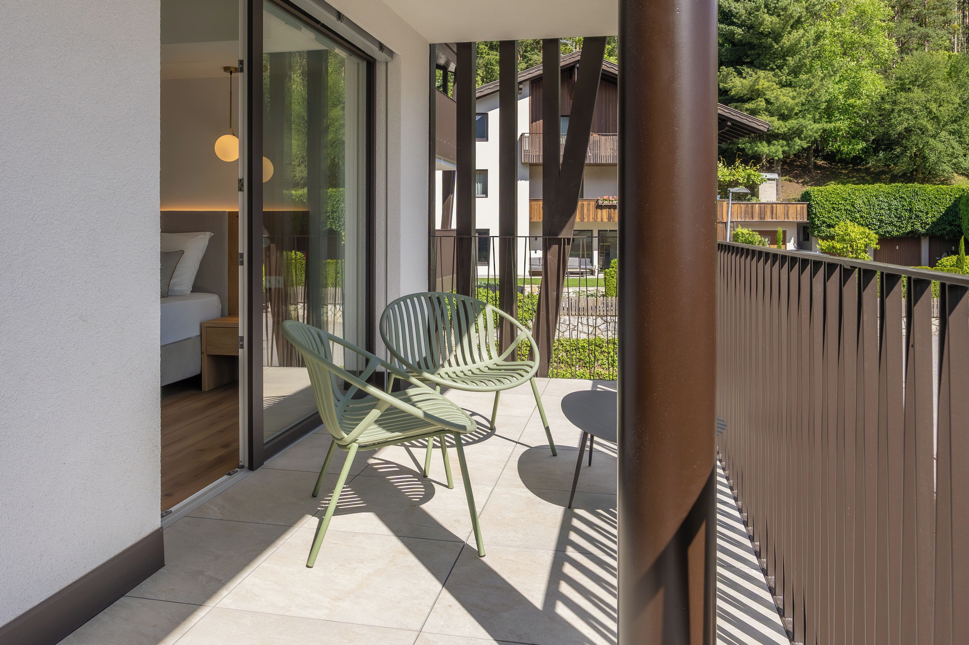 A balcony with two chairs, a table, and a view of a building with balconies and greenery.