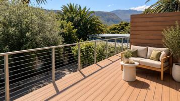 Um deck de madeira com um sofá e uma mesinha, rodeado por vegetação e vista para montanhas.