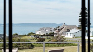 A view from a balcony overlooking a coastal area with houses, a body of water, and distant mountains. - Whale Away Guest House (Hermanus)