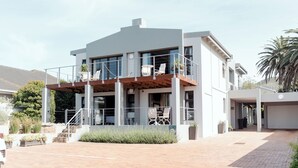 A modern two-story building with a covered outdoor seating area and a garage. - Whale Away Guest House (Hermanus)