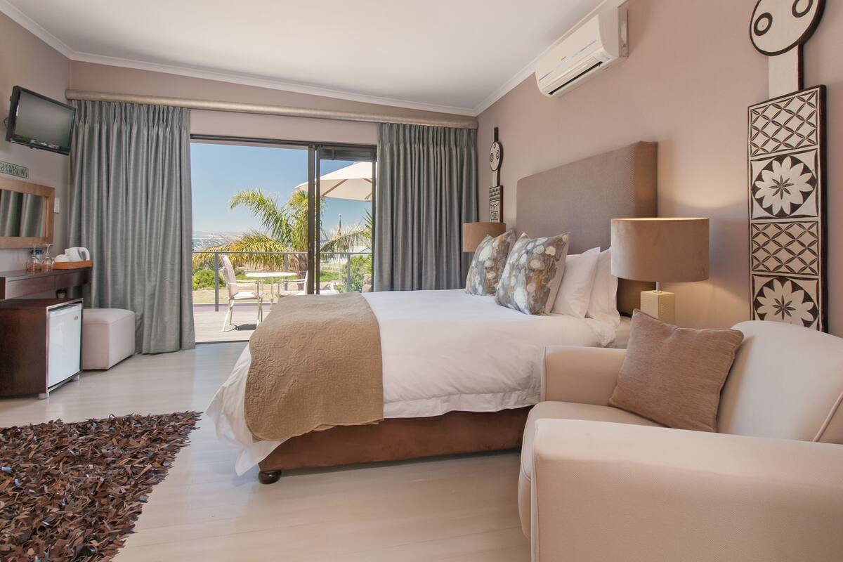 Ein Hotelzimmer mit Bett, Sofa, Schreibtisch, Fernseher und einem Balkon mit Blick.