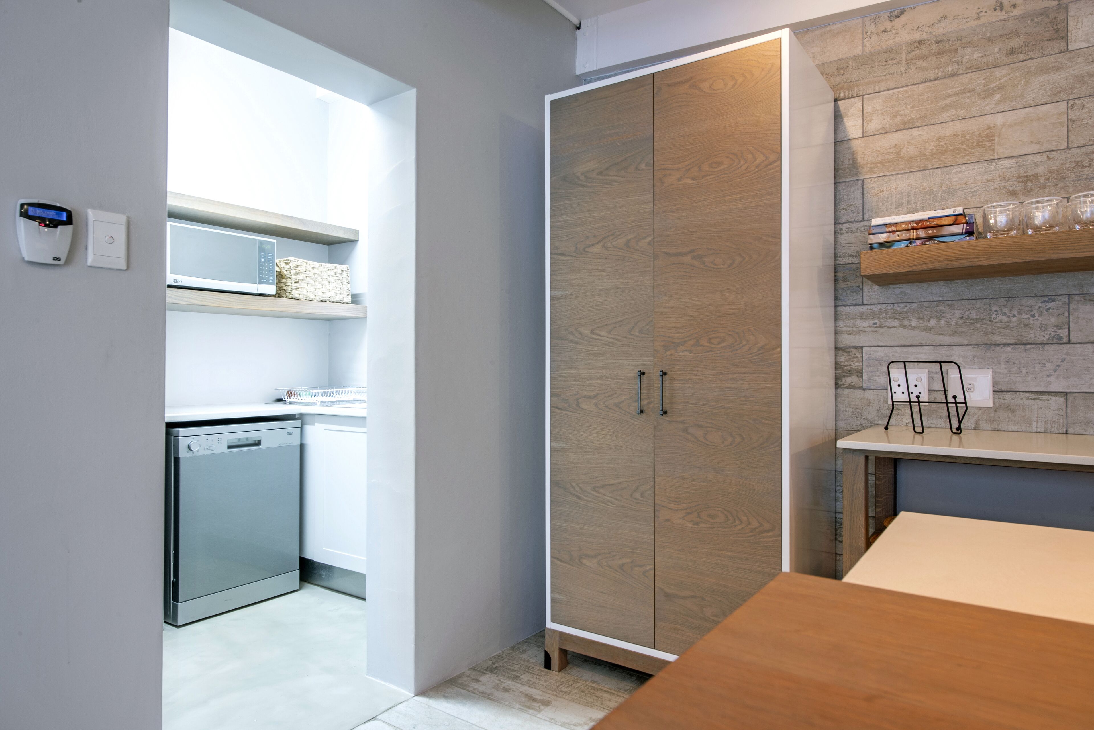 A modern kitchen with a dishwasher, a wooden wardrobe, and a countertop with a glass set.