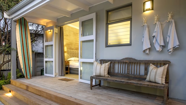 Una terraza de madera con un banco y una tabla de surf apoyada en la pared.