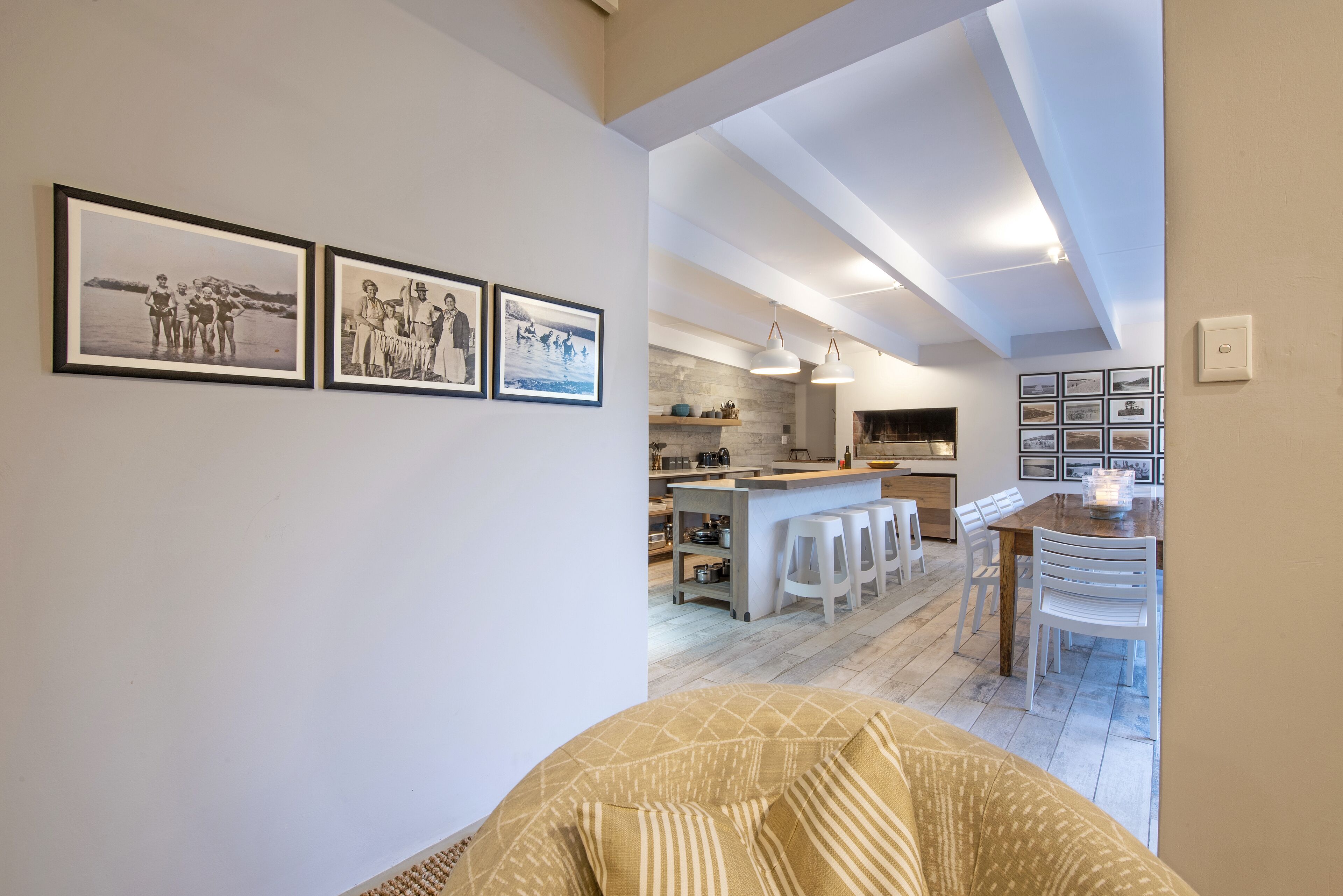 Una cocina moderna con taburetes blancos, una mesa de comedor de madera e iluminación colgante.