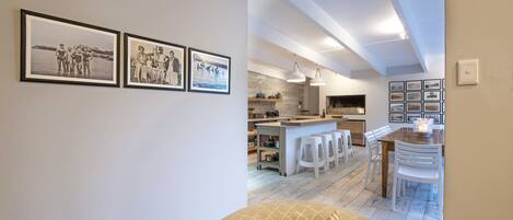 Una cocina moderna con taburetes blancos, una mesa de comedor de madera e iluminación colgante.