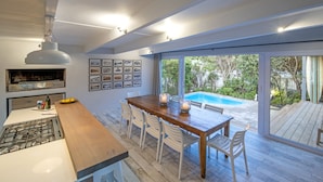 Una cocina moderna con una mesa de madera y sillas blancas, un horno empotrado y un ventanal con vistas a una piscina.