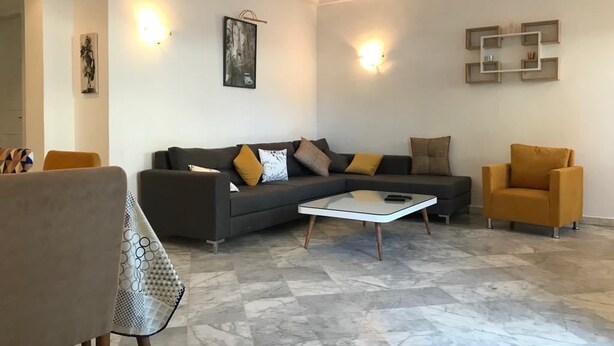 Un salon moderne avec un canapé d’angle, une table basse en verre et un fauteuil jaune.