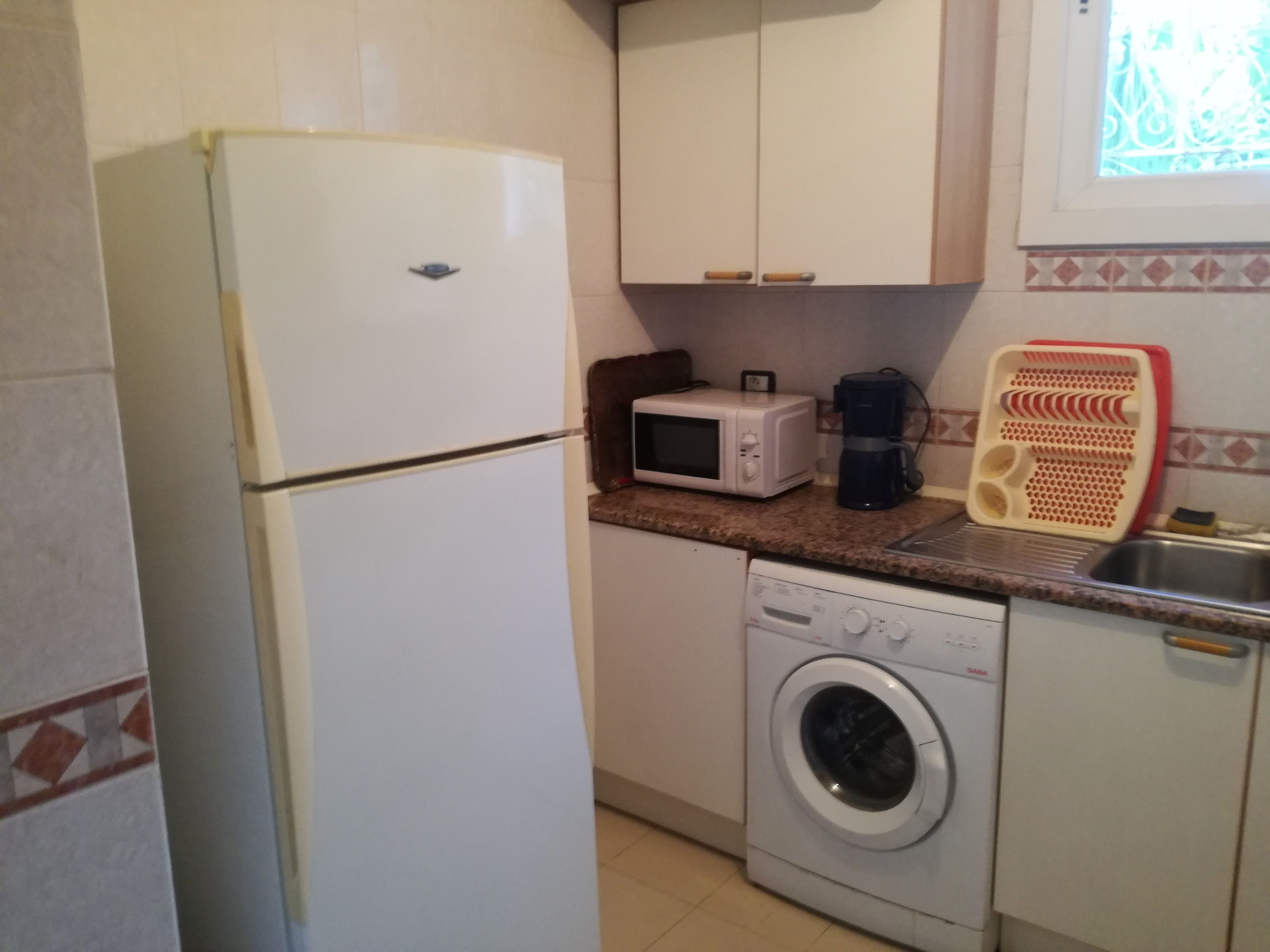 A compact kitchen with a refrigerator, microwave, coffee maker, and washing machine.