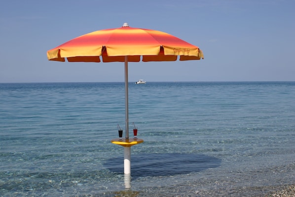 A beach umbrella with a clear view of the sea and a boat in the distance.