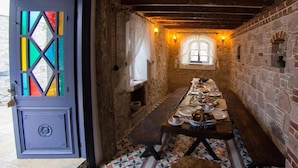 A narrow stone-walled corridor with a long wooden bench and a table set for dining, leading to a window with curtains. - CavliHane 1885 (Ayvalik)