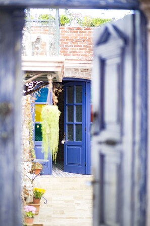 A narrow alleyway with a blue door, potted plants, and a brick wall. - CavliHane 1885 (Ayvalik)