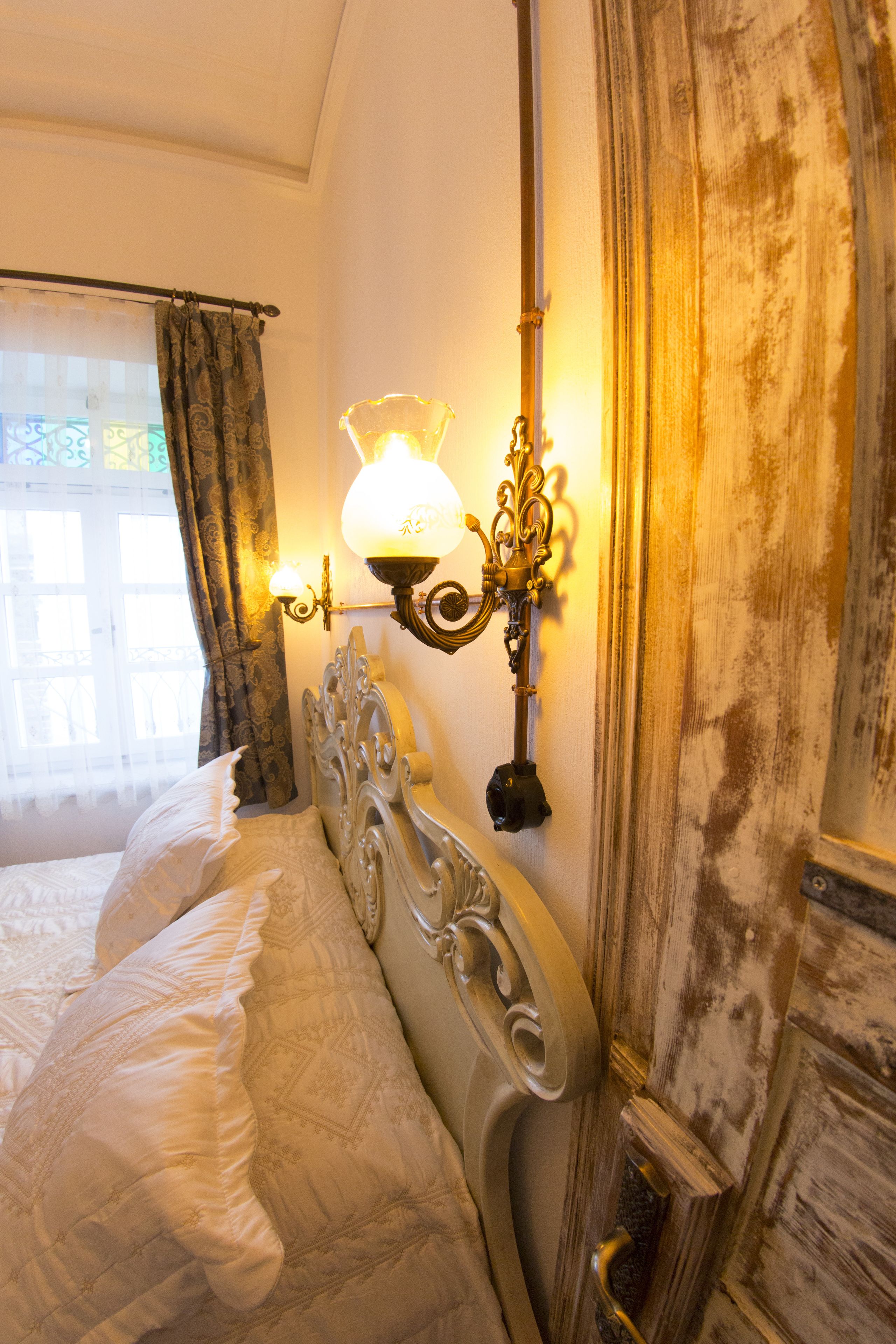 A bedroom with a bed, ornate wall sconces, and a window with curtains.