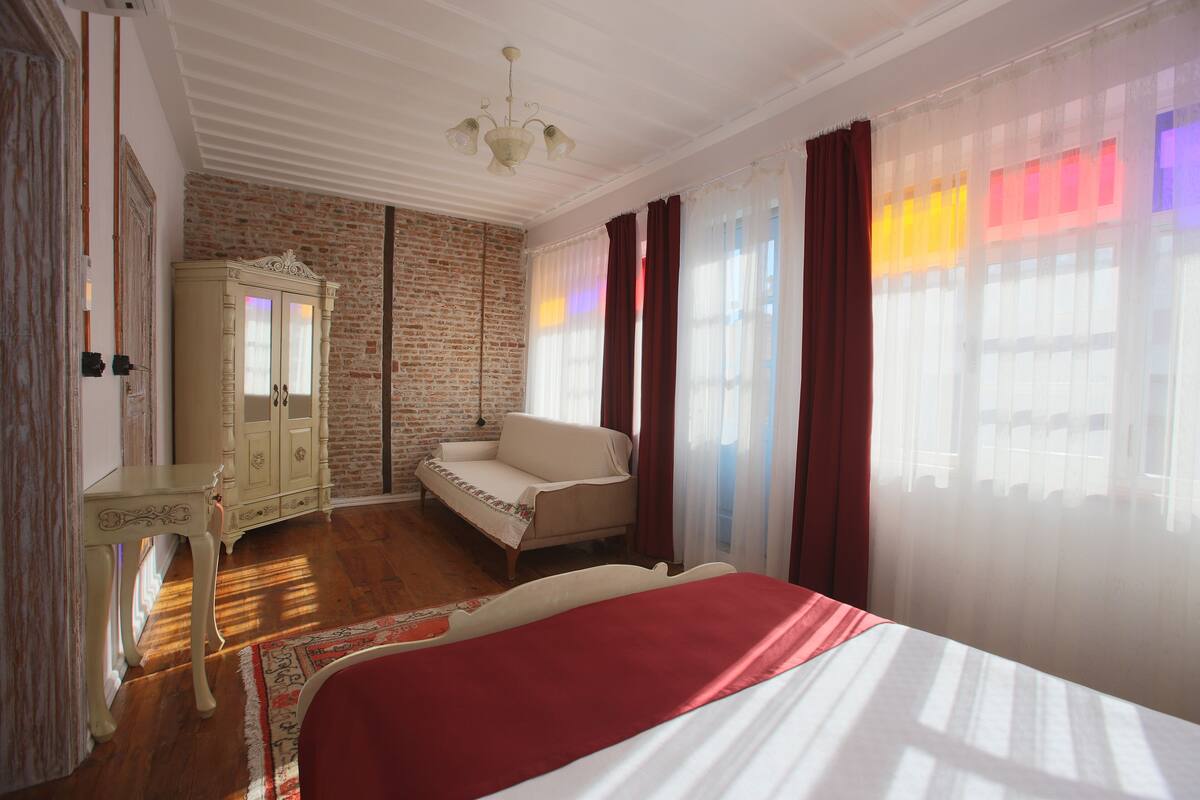 A bedroom with a bed, a sofa, a wardrobe, and a window with curtains.