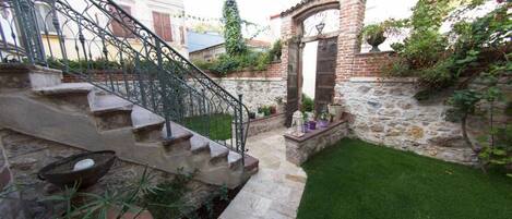 A stone staircase leading to a door, a small garden with a lawn, and a brick wall with climbing plants.