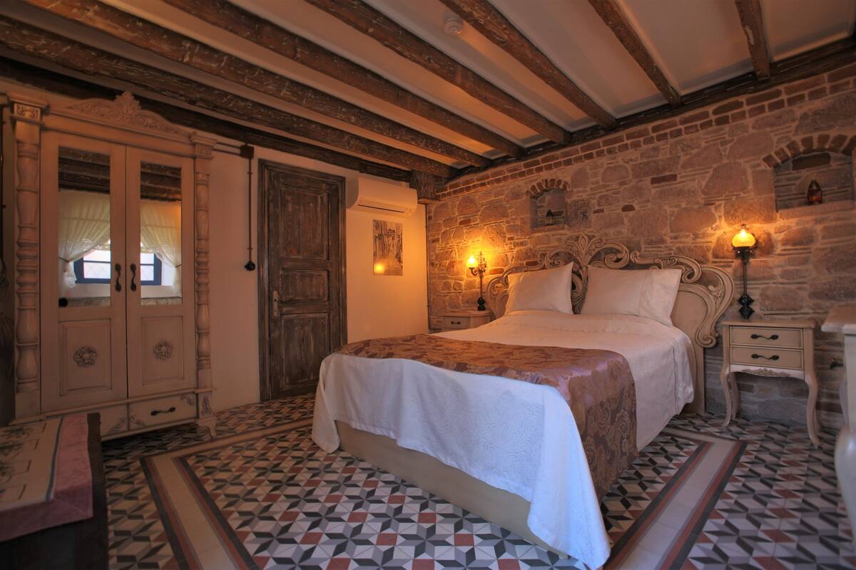 A traditional bedroom with a large bed, a wooden wardrobe, and a stone wall.