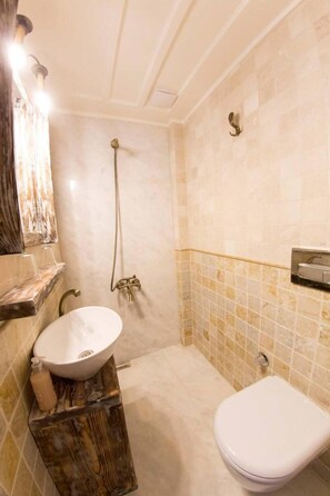 A bathroom with a marble sink, a wooden vanity, a white toilet, and a shower with a handheld showerhead. - CavliHane 1885 (Ayvalik)