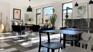 Un comedor moderno con suelo de cuadros, sillas blancas y negras, e iluminación colgante.