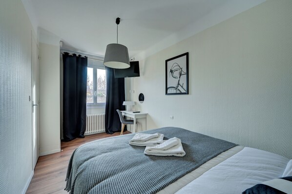 Quarto moderno com cama grande, escrivaninha e janela com cortinas.