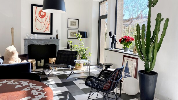 Una sala de estar moderna con piso a cuadros, chimenea, amplio ventanal con vista y una planta de cactus.