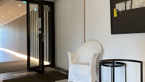 Un moderno vestíbulo de hotel con piso a cuadros, un sillón blanco, una mesita de noche negra y un cuadro abstracto grande en la pared.