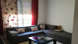 Ein Wohnzimmer mit einem grauen Sofa, einem Glastisch und einem Teddybären auf der Armlehne.