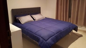 Ein Bett mit grauem Kopfteil und blauer Bettdecke.