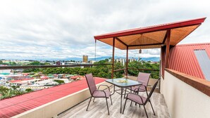 A balcony with a table and chairs, a red roof, and a view of a cityscape. - Hotel Castillo (San José)