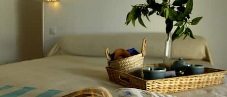 A neatly made bed with a basket of fruits, a vase with a plant, and a magazine on the bed.