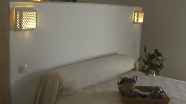 A bedroom with a bed, a bedside table with a plant, and a wall-mounted light fixture. - La Chambre Verte (Sidi Bou Said)