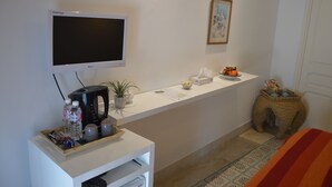 A clean, modern hotel room with a flat-screen TV, a coffee maker, a small plant, and a basket of toiletries. - La Chambre Verte (Sidi Bou Said)