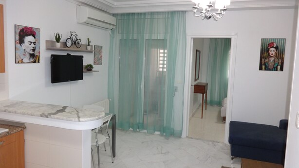 A modern living room with a marble floor, a TV mounted on the wall, a bicycle, and a blue sofa.