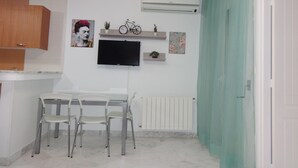 A modern kitchen with white cabinets, a dining table with chairs, a mounted TV, and decorative items on shelves.