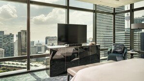 A modern hotel room with a large TV on a glass table, a comfortable bed, and a city view through large windows. - Four Seasons Hotel Kuala Lumpur (Kuala Lumpur)