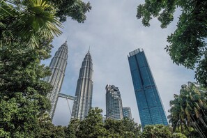 Vista de las Torres Petronas y un moderno rascacielos, rodeados de frondosos árboles verdes.