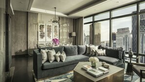 Un salon moderne avec un canapé gris, une table basse et une vue sur la ville grâce à de grandes fenêtres.