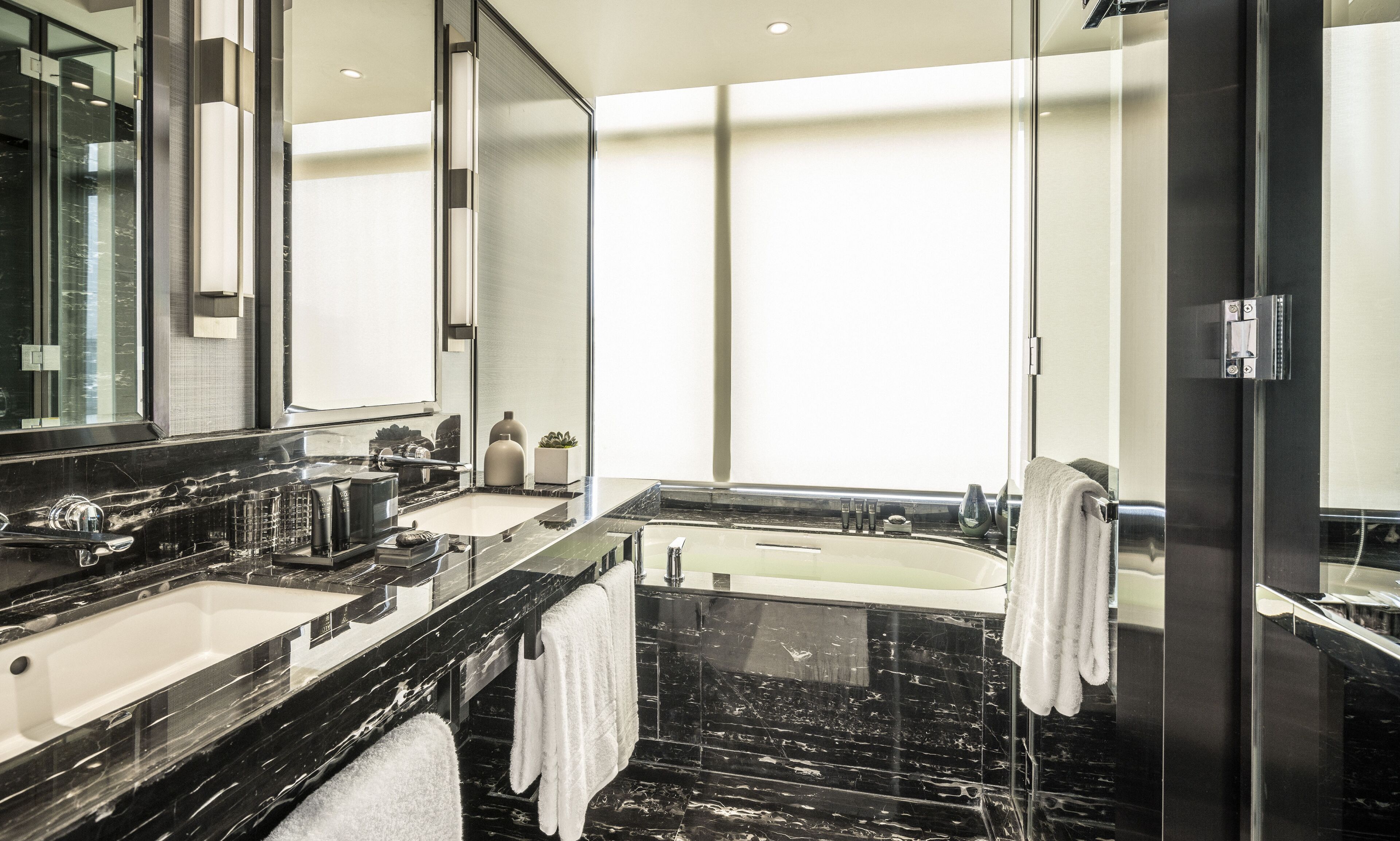 A modern bathroom with a large mirror, two sinks, a bathtub, and a glass shower enclosure.