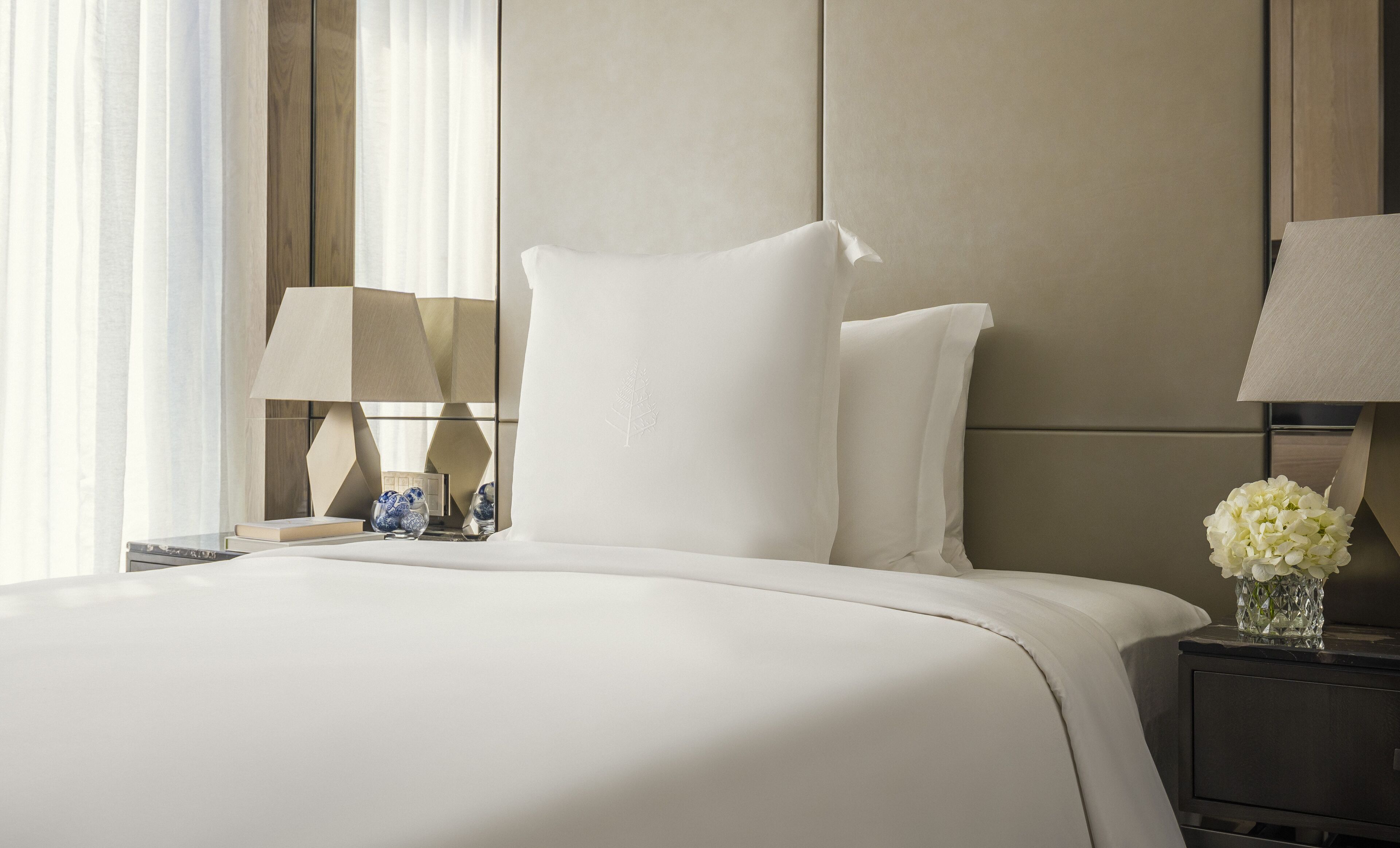 A hotel room with a large bed, two bedside tables, and a nightstand with a vase of flowers.