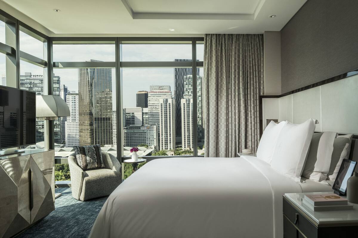 Une chambre d’hôtel moderne, dotée d’un grand lit, d’un bureau, d’une chaise et offrant une vue sur le paysage urbain.