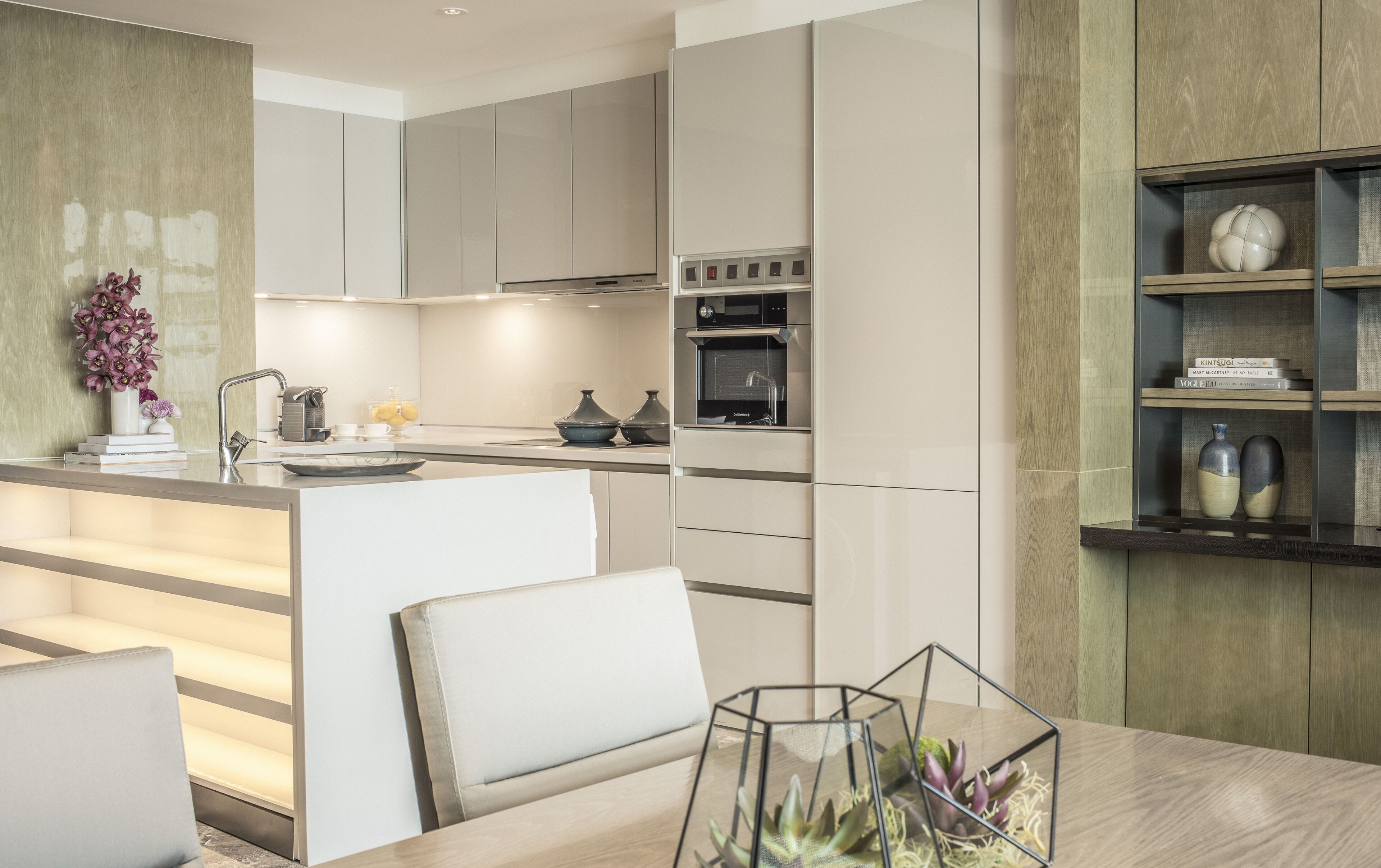 Una cocina moderna con electrodomésticos integrados, un comedor con mesa de vidrio y una estantería de madera.