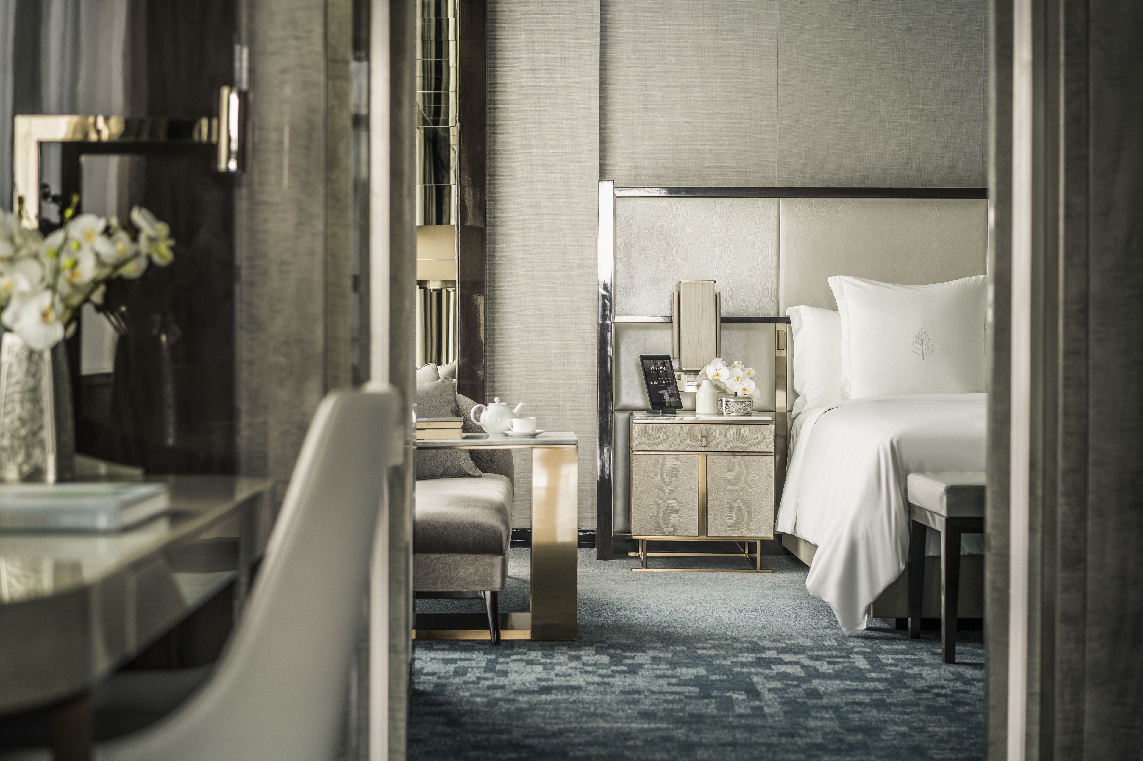 A modern hotel room with a large bed, a bedside table with a lamp, a small desk, and a chair.
