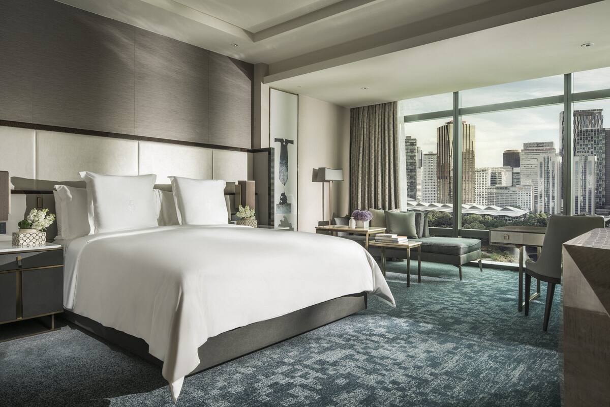 Une chambre d’hôtel moderne, dotée d’un grand lit, d’un bureau et offrant une vue sur le panorama urbain.