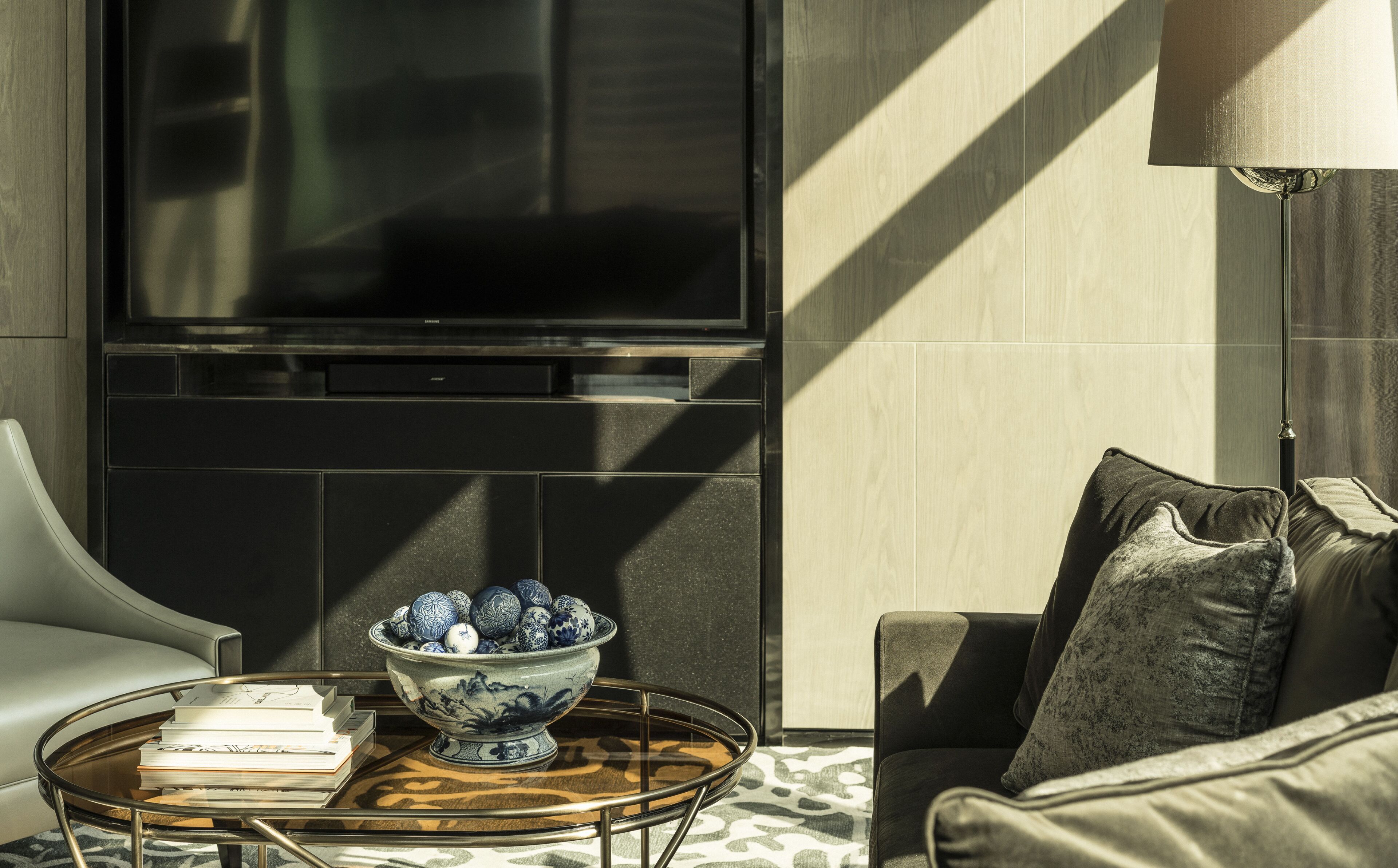 A modern living room with a sofa, a coffee table with a bowl of decorative eggs, and a flat-screen TV mounted on the wall.