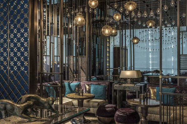 Un interior lujoso de diseño moderno, con una zona de estar que incluye sofás, otomanas, una mesa de centro de vidrio y una escultura decorativa.