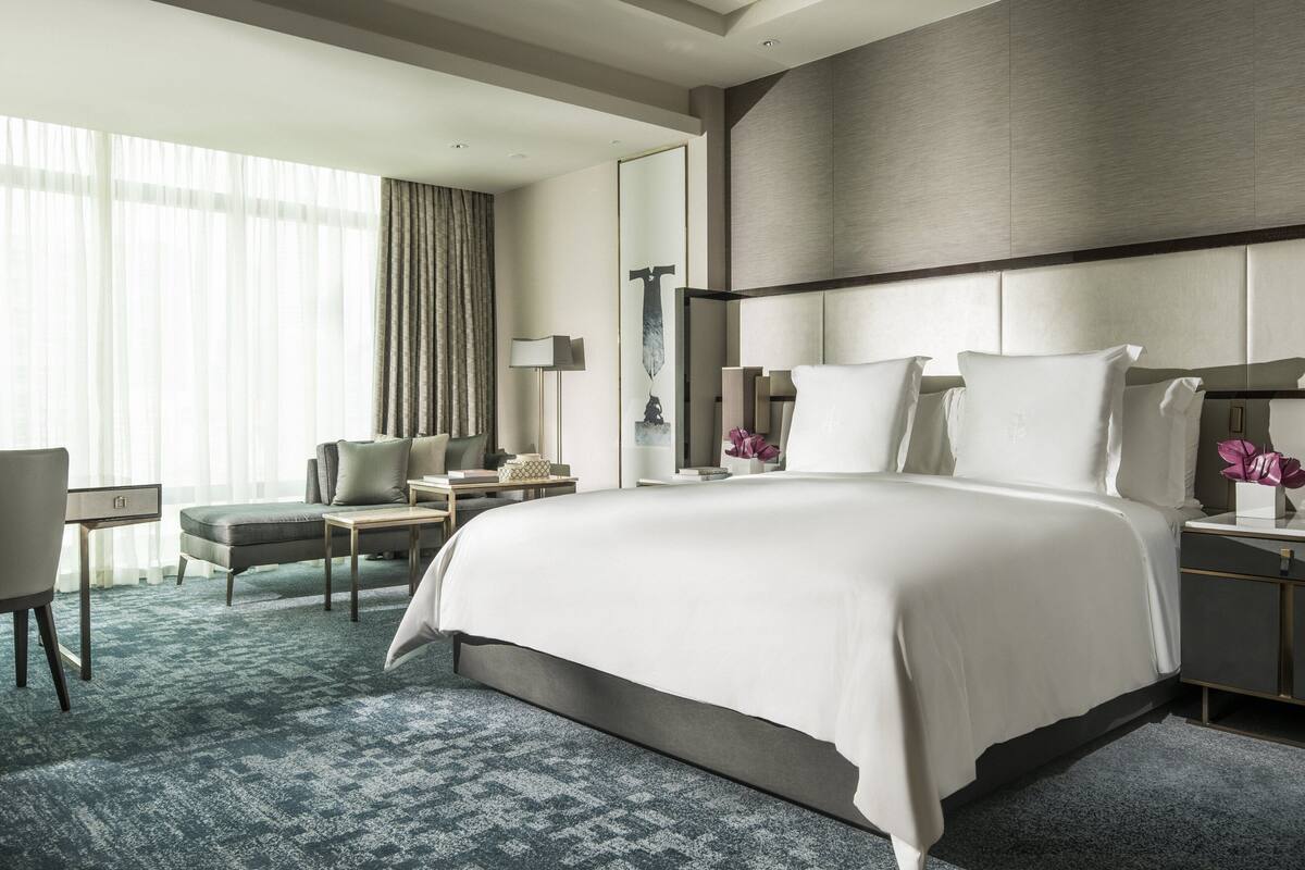 Une chambre d’hôtel moderne avec un grand lit, un bureau, une chaise et une grande fenêtre avec des rideaux.