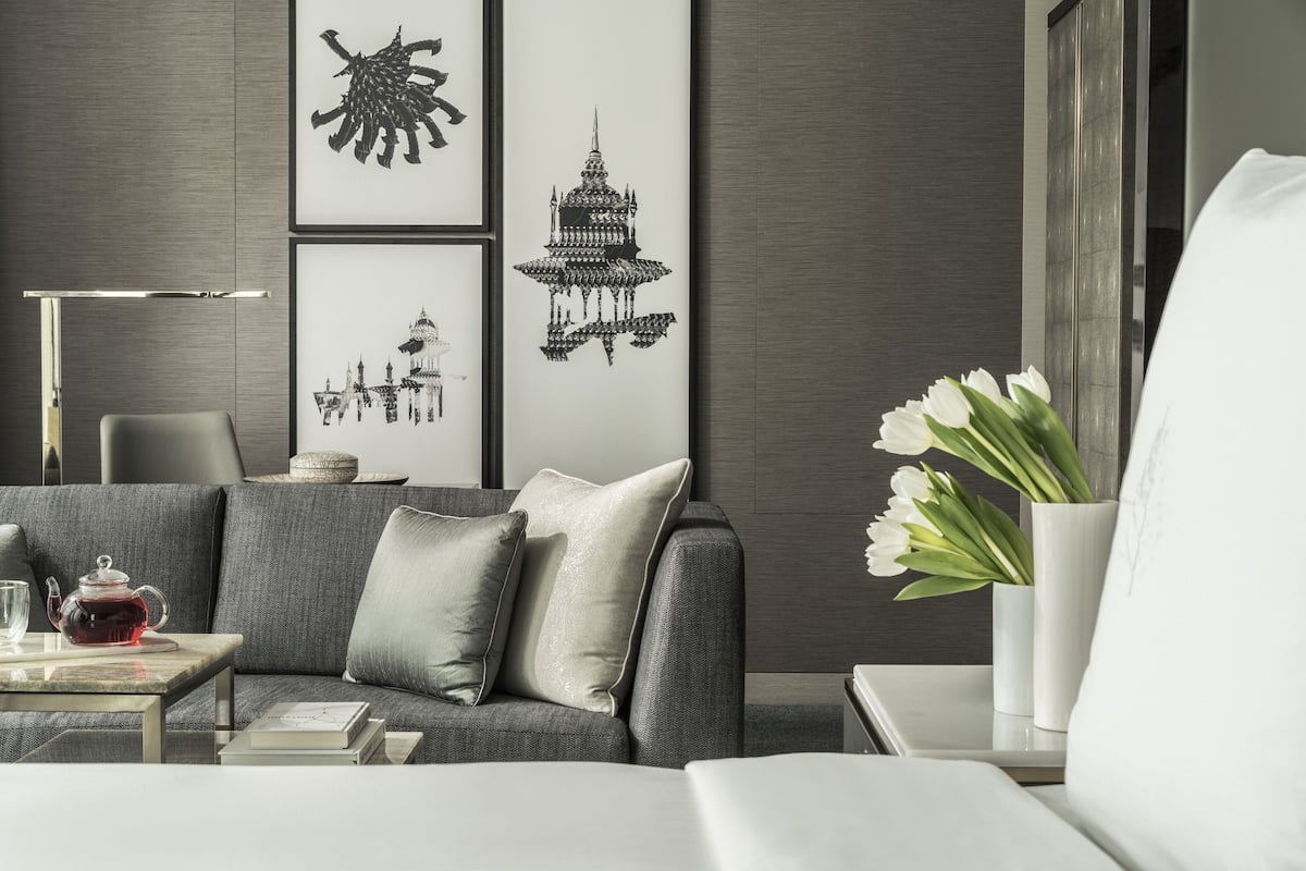 Un salon moderne avec un canapé gris, une table en verre sur laquelle se trouve une théière, et un vase rempli de fleurs blanches.