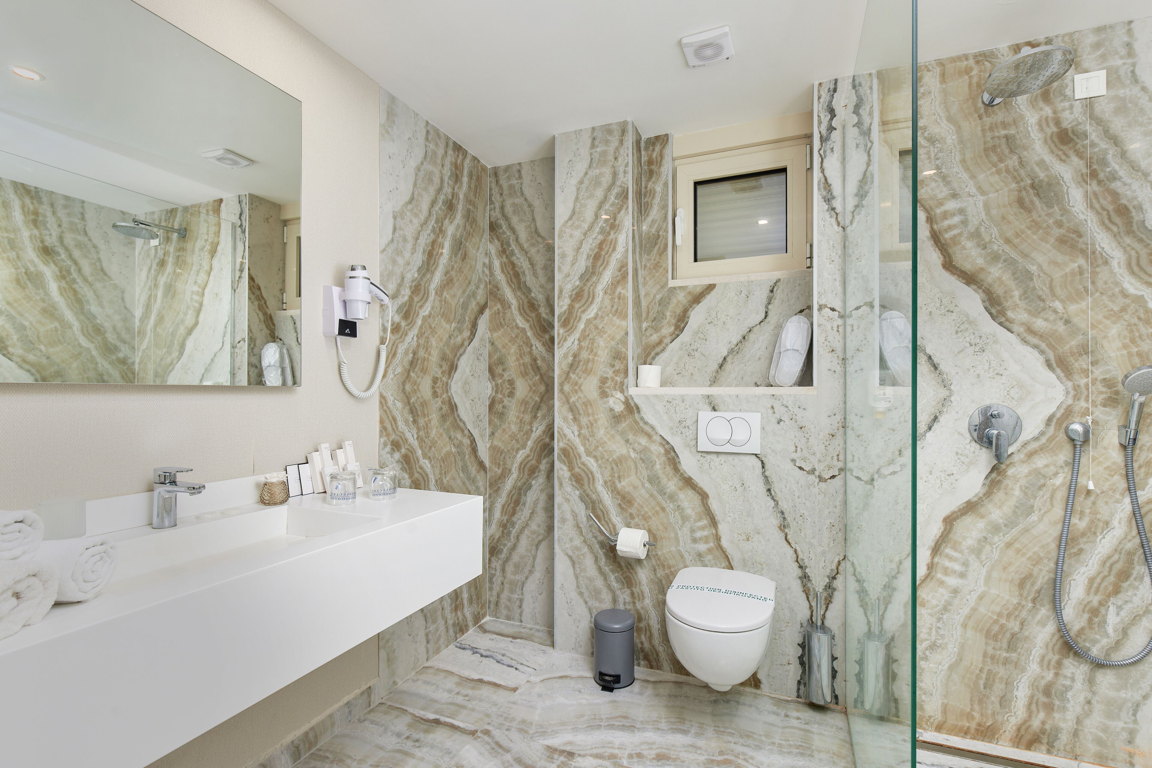 Une salle de bain moderne avec un pare-baignoire en marbre, un lavabo blanc, une douche en verre et des toilettes.